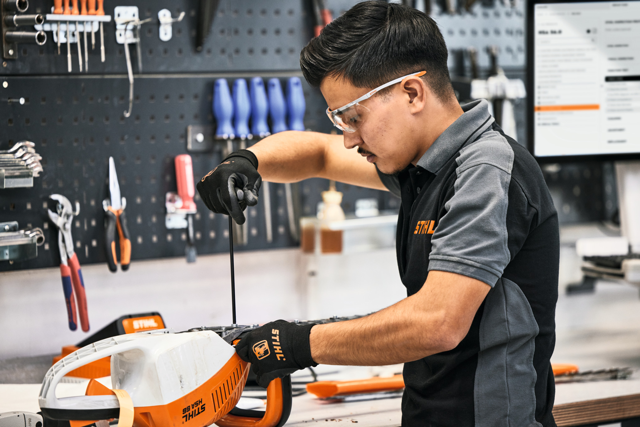A man performing maintenance work on a STIHL hedge trimmer in the work shop