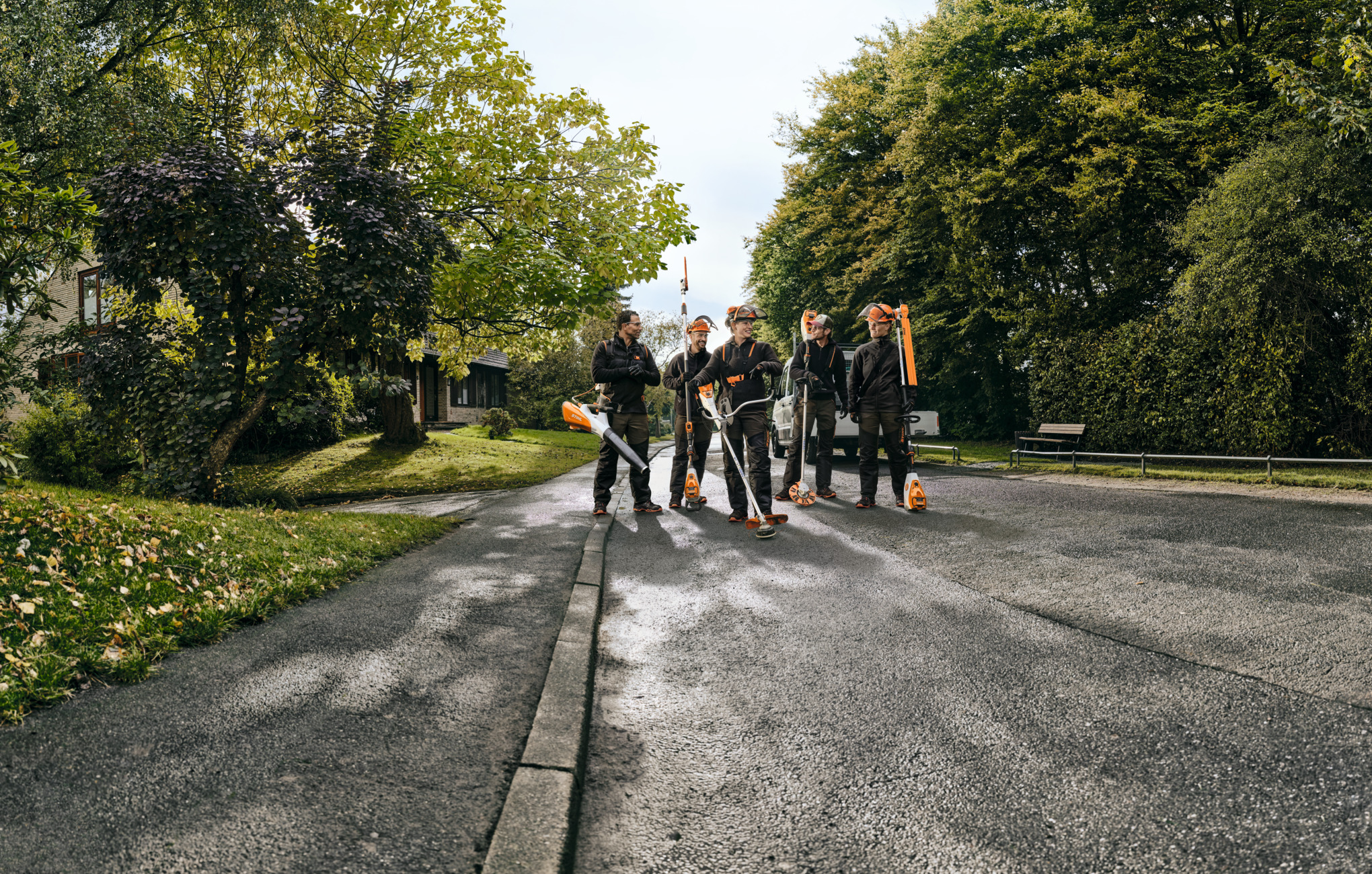 Five STIHL professionals walking along a road holding battery power tools