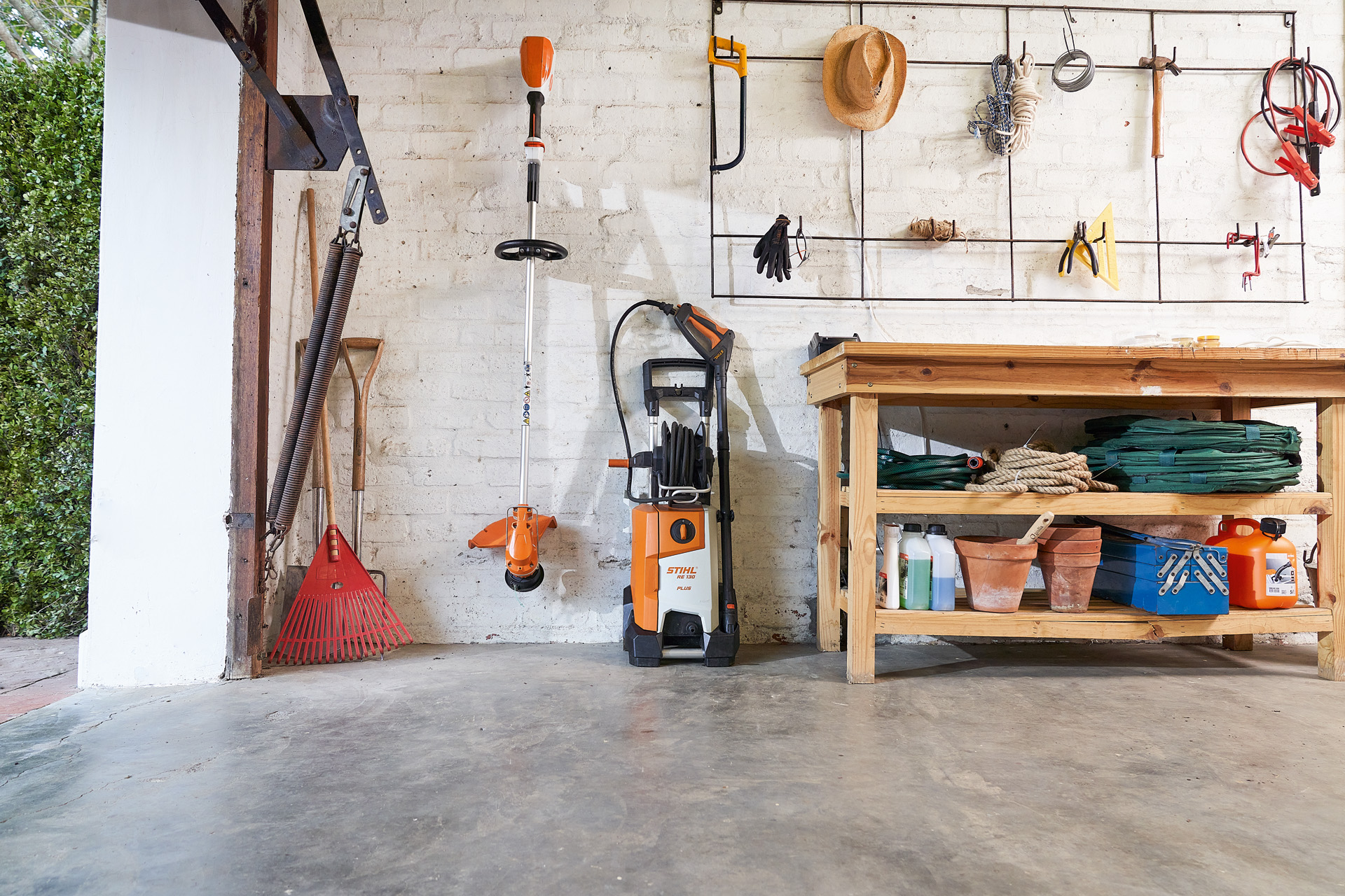 A STIHL RE 130 Plus high-pressure cleaner and a STIHL brushcutter stored beside garden tools in a garage 