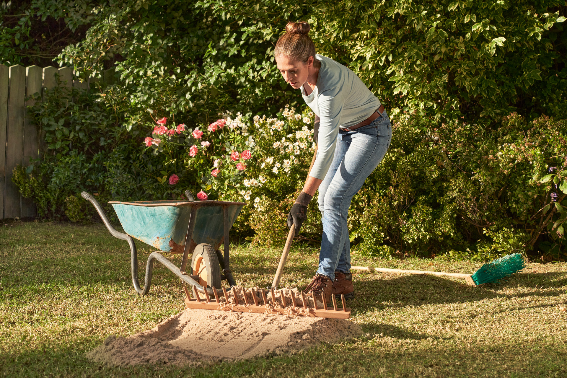 A woman sanding her lawn with a wheelbarrow in the background