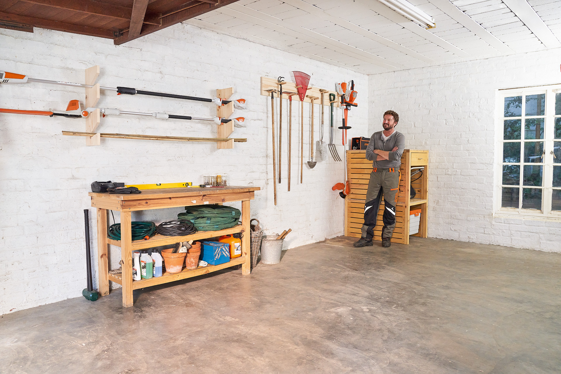 A man with arms folded leaning next to a DIY hanging garden tool storage rack in a garage