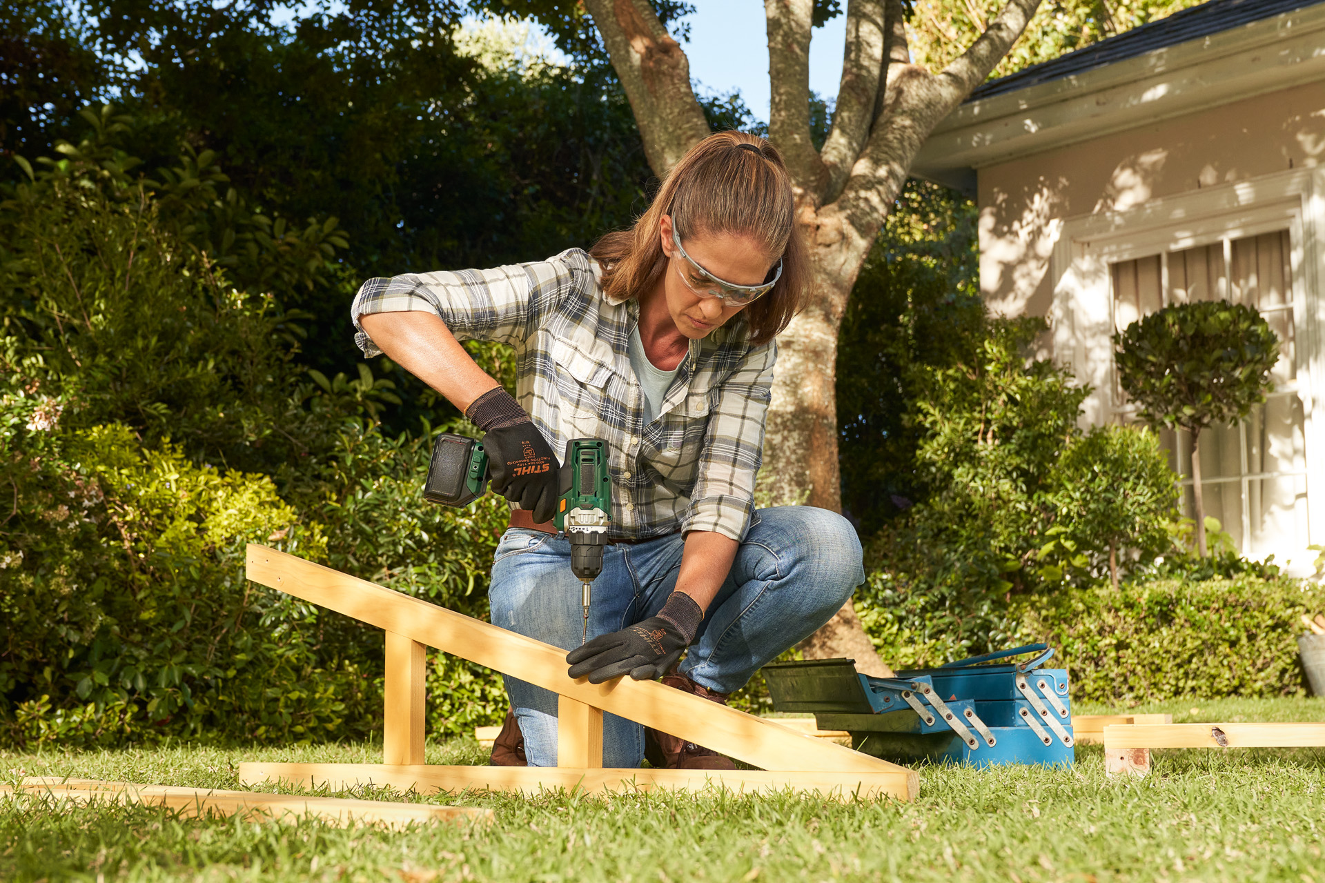 A person wearing STIHL protective gloves using a battery drill on a wooden beam