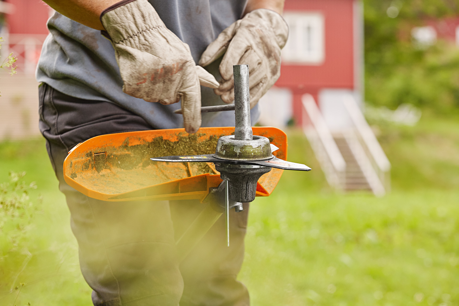 A grass trimmer being held upside down as someone wearing gloves inspects the metal cutting tool