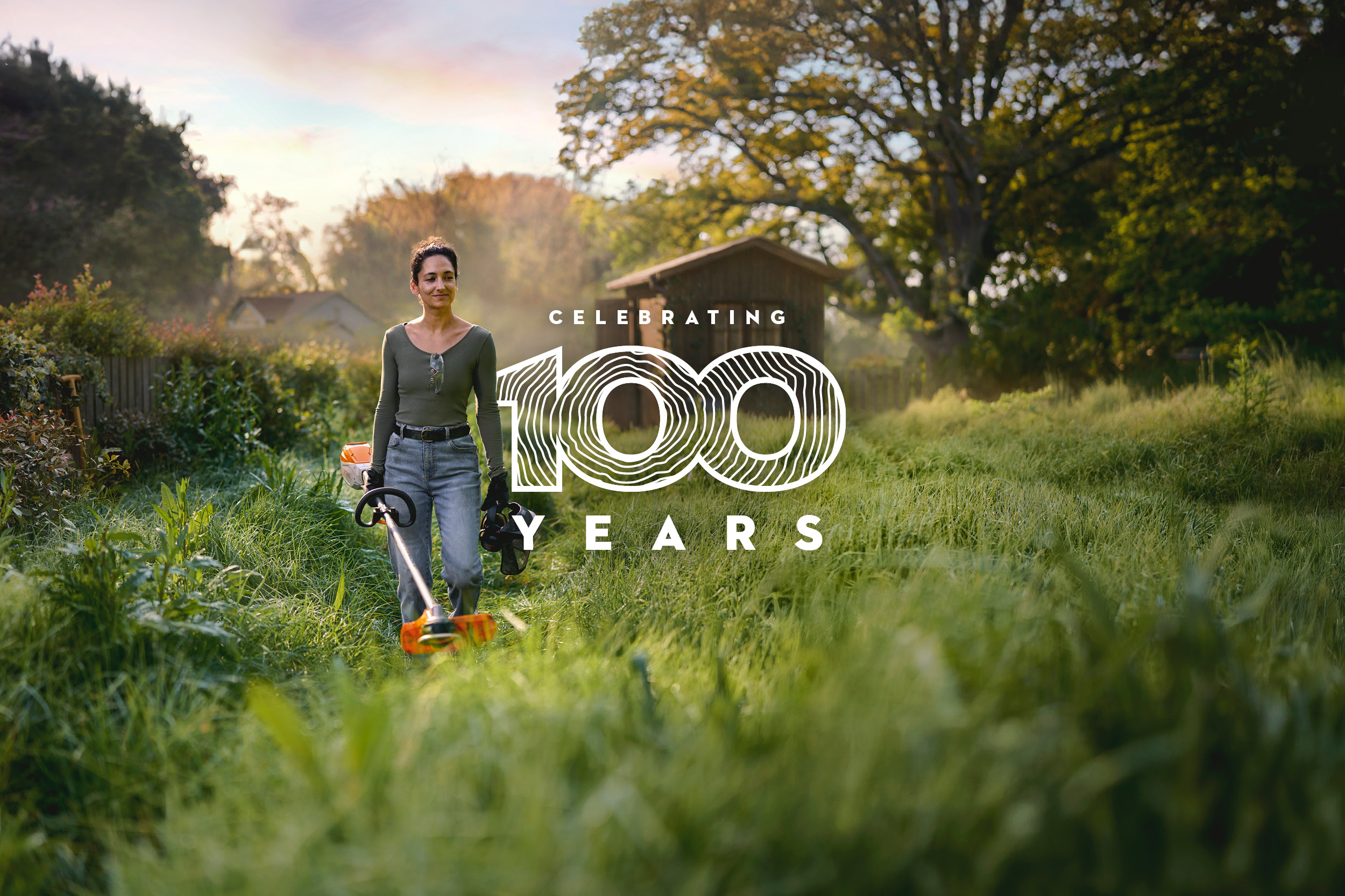 A women carrying a STIHL grass trimmer through grass