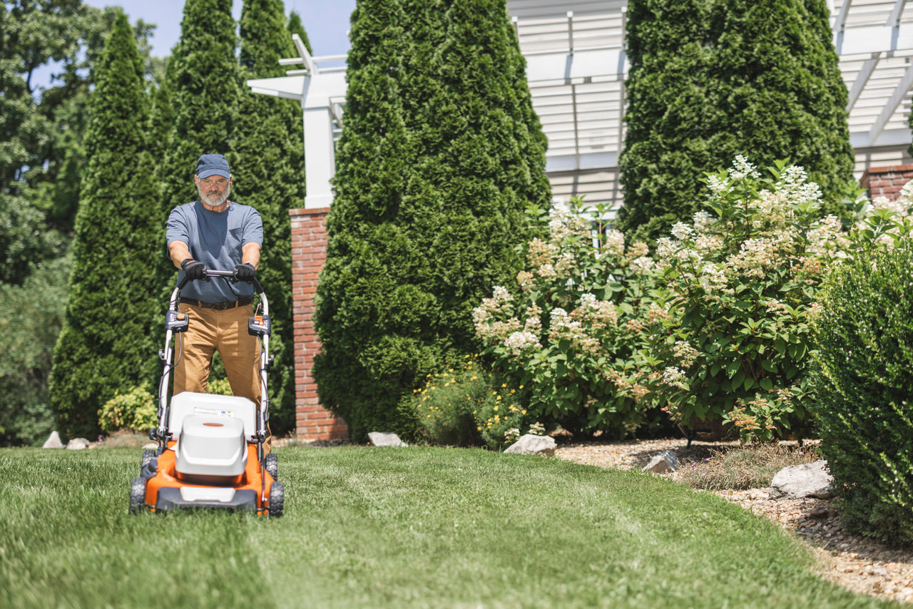 Woman treats her lawn in spring with a STIHL RM 243 T petrol lawnmower in the garden in front of a house