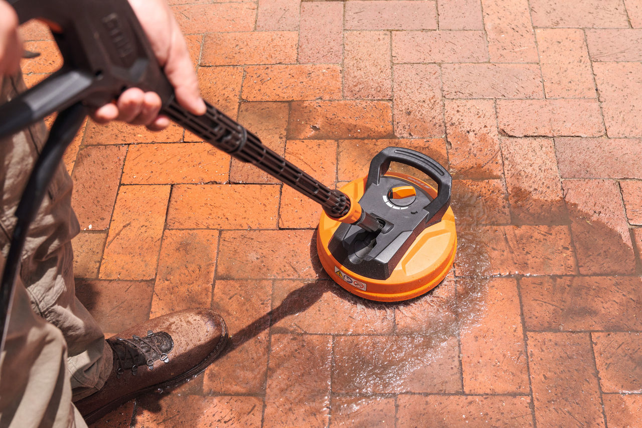 Person adding STIHL CS 100 Stone and Facade cleaner to foam nozzle to clean paving stones